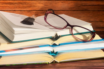 On a wooden surface are open books with women's glasses for sight.
