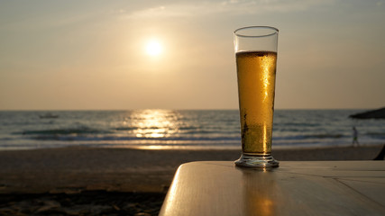 Cold beer in a glass at sunset, sea and beach in the background.
