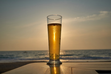 Glass of a cold beer at sunset, sea and beach in the background.