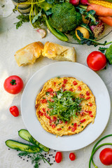 egg omelet with cherry tomatoes, cheese and arugula on a plate on the table with a white tablecloth
