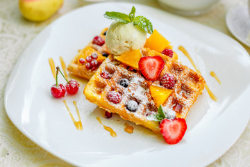 Belgian waffles with ice cream and fruits and berries on a white plate