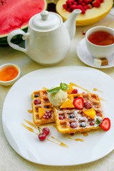 Belgian waffles with ice cream and fruits and berries on a white plate