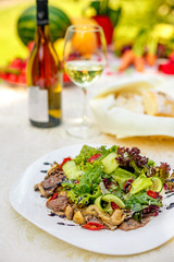 warm salad with meat, cucumber and vegetables on a white plate on the table