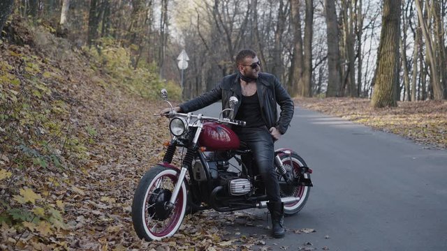 Portrait of stylish biker behind a motorcycle in autumn park