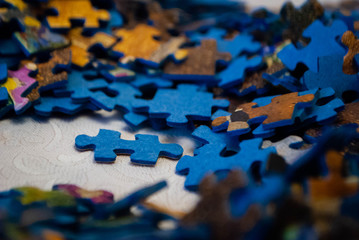 Close-up of colorful pieces of puzzle. One standing puzzle piece on the table. Stack of Puzzle Pieces. Puzzle pieces. Puzzle figures. Puzzle for fun.  - obrazy, fototapety, plakaty