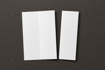 Blank vertical A4 leaflet on black wooden background. Bi-fold or half-fold opened and folded brochure isolated with clipping path. View directly above. 3d illustration
