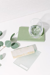 Glass of water, notebook, and tile and glass samples with eucalyptus leaves on white surface / modern interior design remodel concept