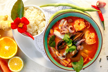 Thai soup tom yam with seafood (octopus, shrimps), herbs and vegetables served on the table with ingredients, healthy food