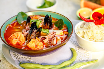 Thai soup tom yam with seafood (octopus, shrimps), herbs and vegetables served on the table with ingredients, healthy food
