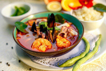 Thai soup tom yam with seafood (octopus, shrimps), herbs and vegetables served on the table with ingredients, healthy food