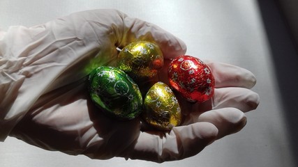 hand wearing latex glove offering colorful chocolate easter eggs