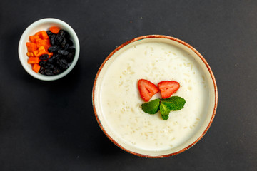 rice porridge with milk, healthy breakfast with raisins, nuts, mint on a white plate