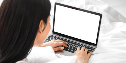 Young asian woman relaxing using laptop computer with white mockup blank screens in the bedroom at home. Young creative girl working and typing on keyboard.work from home concept