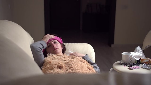 sad woman is sick alone at home, lies on the couch in the evening, fever, self-medication, self-isolation