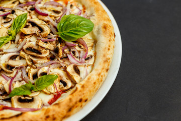 delicious Italian pizza with parmesan cheese, mushrooms, onions and basil on a black table