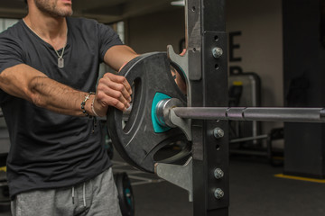 Cropped image of a man putting heavy disk on a barbell. Selective focus