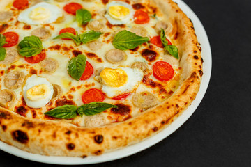 delicious Italian pizza with chicken sausages, eggs and basil on a black table