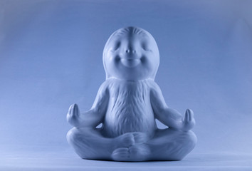 Blue smiling and calm looking sloth ornament sitting in the lotus meditating position 