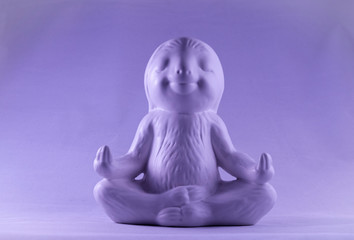 Purple smiling and calm looking sloth ornament sitting in the lotus meditating position 