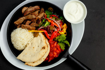 fried beef in a pan with rice, pita and vegetables