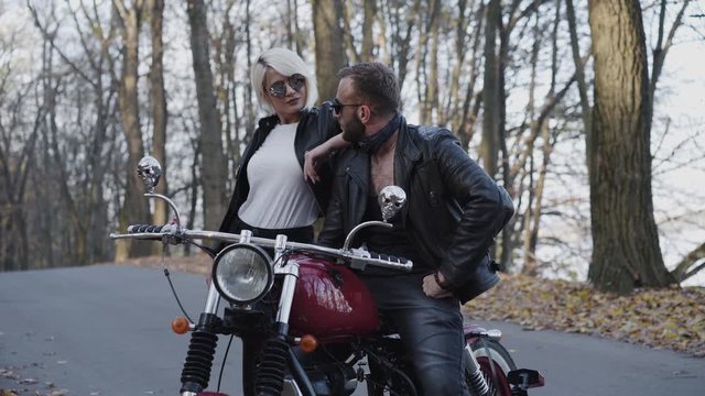 Portrait of biker couple stands in pose at motorcycle in forest