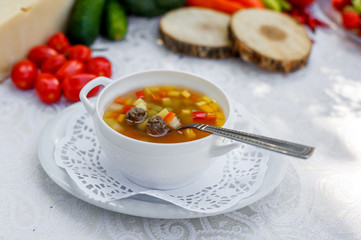 vegetable soup with meatballs in a white plate on a white tablecloth