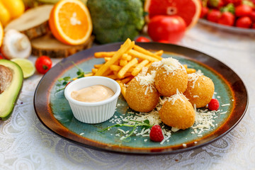 Crispy potato balls with soft melted cheese and french fries on decorated table