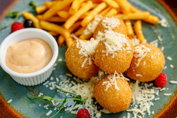 Crispy potato balls with soft melted cheese and french fries on decorated table