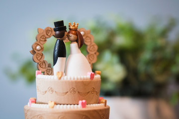 Wooden Groom with top hat and tux kissing bride on wedding cake music box with green plan in the background. Wedding gift and marriage present. Cake decoration and topper and a couple kiss. Newlywed.