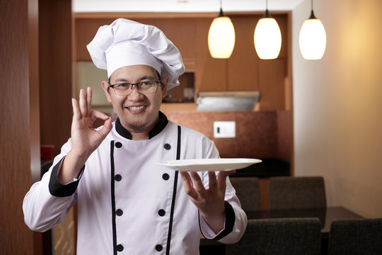 Asian Male Chef Shows Empty White Plate, Presenting Something, Copy Space