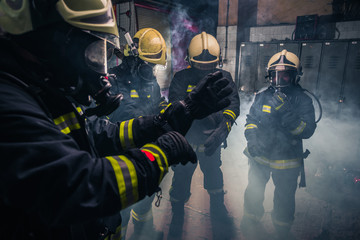 Firemen in uniform wearing gloves and gas masks inside the fire department