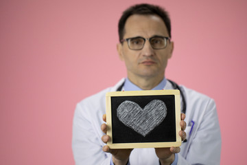 Caucasian doctor epidemiologist with a stethoscope on a pink background holds a heart in his hands. Caring for people or patients. Medical service. Heart disease treatment. Close-up
