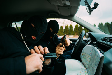 Bank robbers with their masks on pointing at the map prepared for robbing the bank,sitting in the car and waiting for the right time to rob.