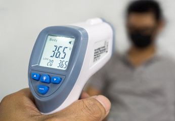 Hand holding infrared thermometer to measuring temperature on blurred asia people with face mask on background. Covid flu screening 19 concept.