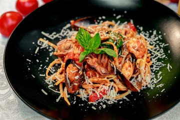 Italian pasta with parmesan cheese and seafood, with octopus, shrimps and mussels in a black plate on a white table