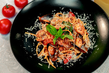 Italian pasta with parmesan cheese and seafood, with octopus, shrimps and mussels in a black plate on a white table