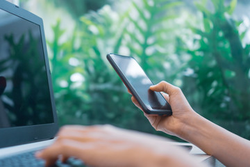 Woman hand using laptop or smartphone to work study on work desk with clean nature background background. Business, financial, trade stock maket and social network.