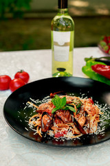 Italian pasta with parmesan cheese and seafood, with octopus, shrimps and mussels in a black plate on a white table