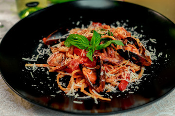 Italian pasta with parmesan cheese and seafood, with octopus, shrimps and mussels in a black plate on a white table