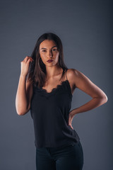 Young beautiful stylish girl posing in studio with one hand on the waist on a gray background