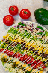 fresh salad with three kinds of meat, avocado, tomatoes and eggs on a white table