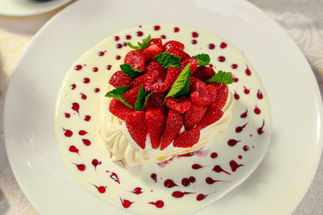 Pavlova dessert with cream mint and strawberry in a white plate on a white table