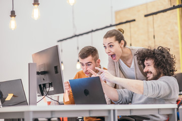 Happy surprise for the teammates. Coworkers cheering while looking at a computer, screen at the office. Positive vibe at the startup modern office.