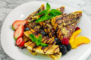 Belgian waffles with nuts, chocolate and fruit on a white plate, beautiful serving