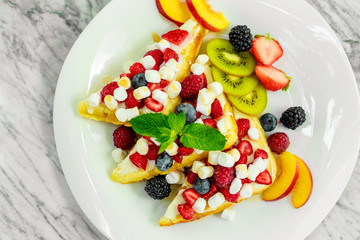Belgian waffles with nuts, chocolate and fruit on a white plate, beautiful serving