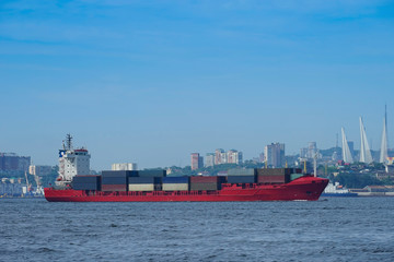 Red container ship on the background of the urban landscape.