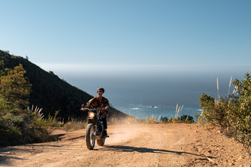 Man riding motorcycle on dirt road against sea