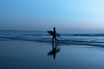 Man with surfboard walking on beach at dusk