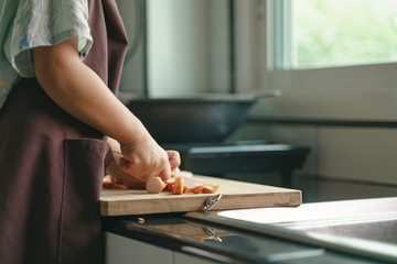 Asian boy cooking by cutting sausage