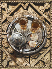 Fototapeta na wymiar Traditional moroccan mint tea with cookies on silver tray on carved wooden table. Beautiful vintage style, hospitality in Morocco.